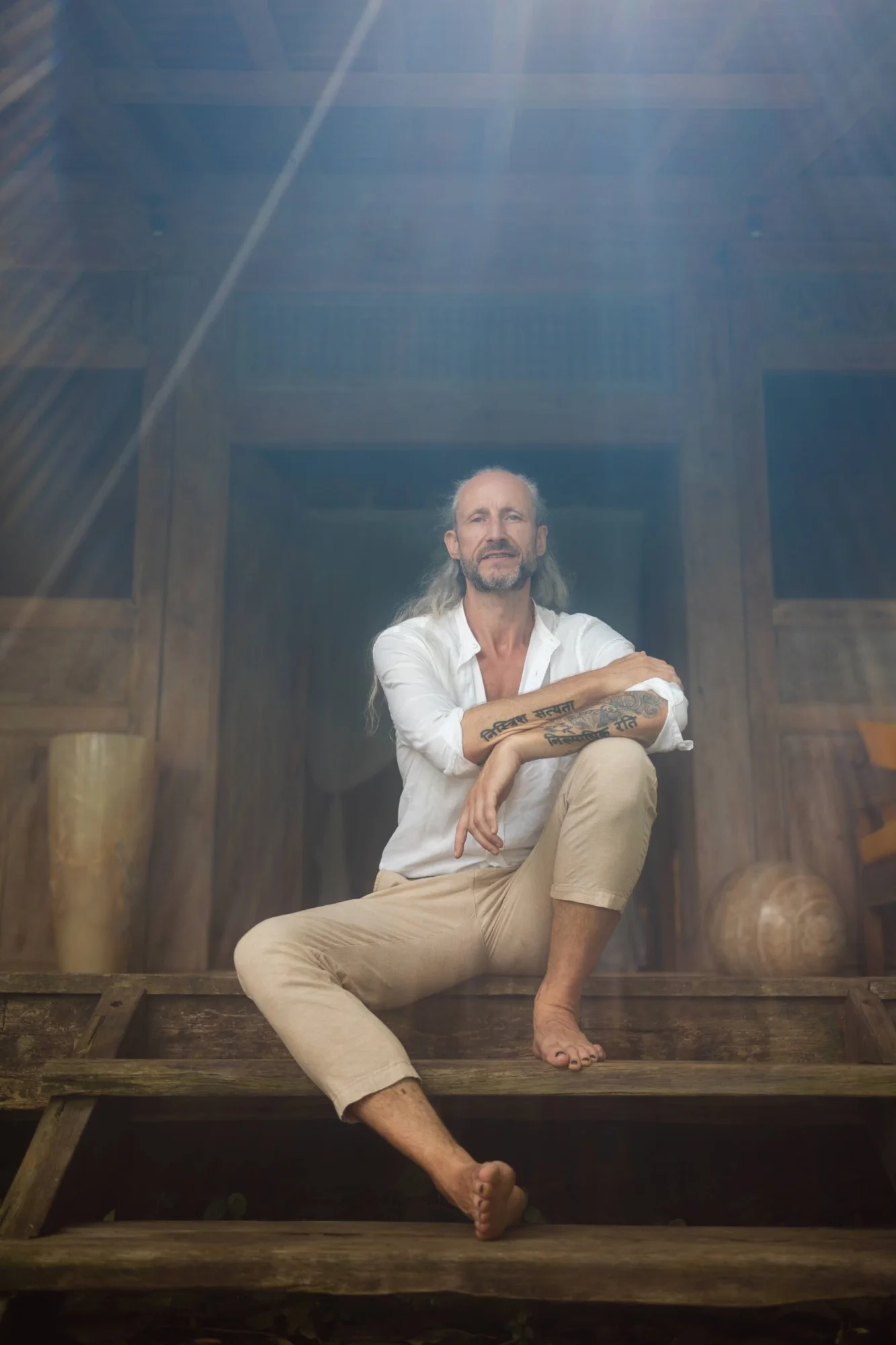 Steve Shiva in a white shirt, sitting on wooden temple steps in shafts of light
