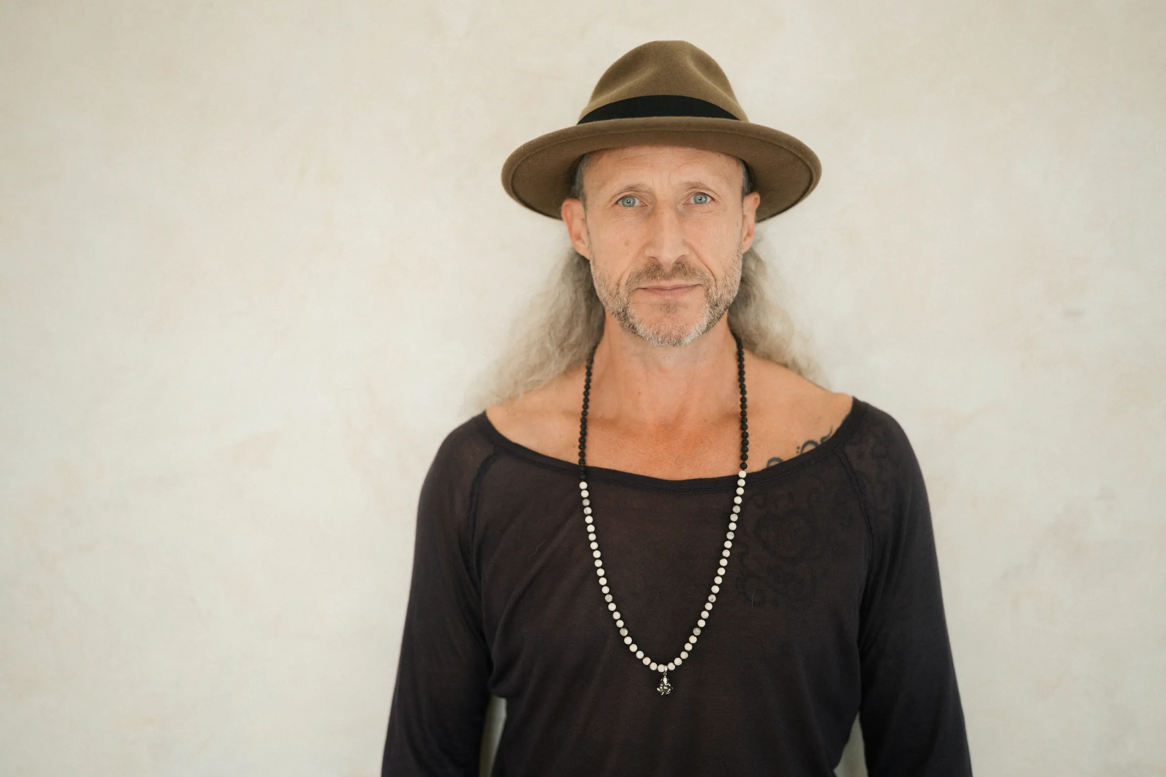 Steve Shiva in a hat against a warm plaster wall