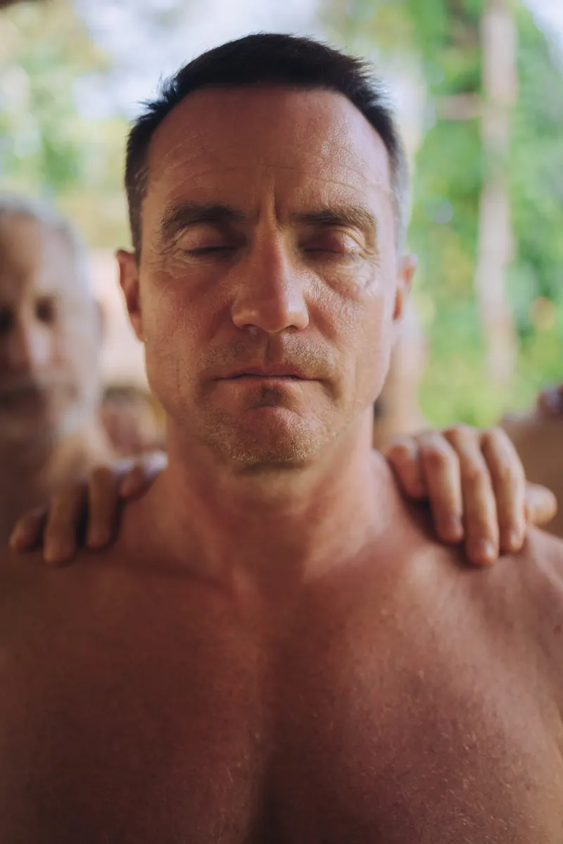 A brother with eyes closed, hands of the men on his shoulders