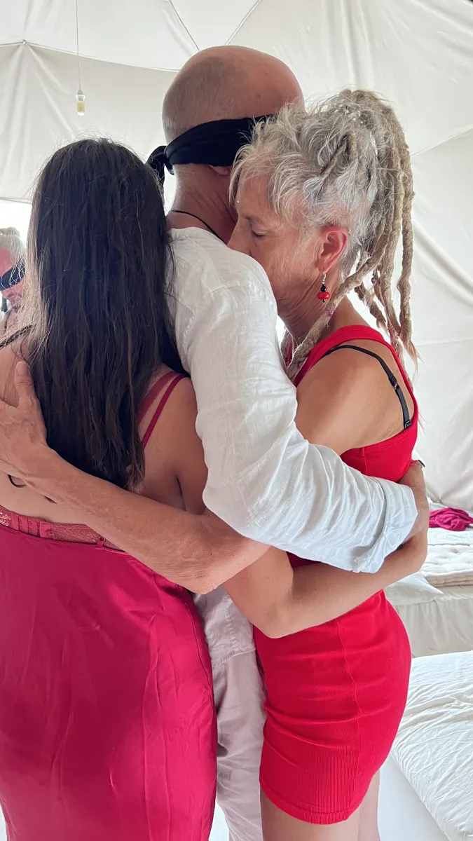 A blindfolded man embraced by the women
